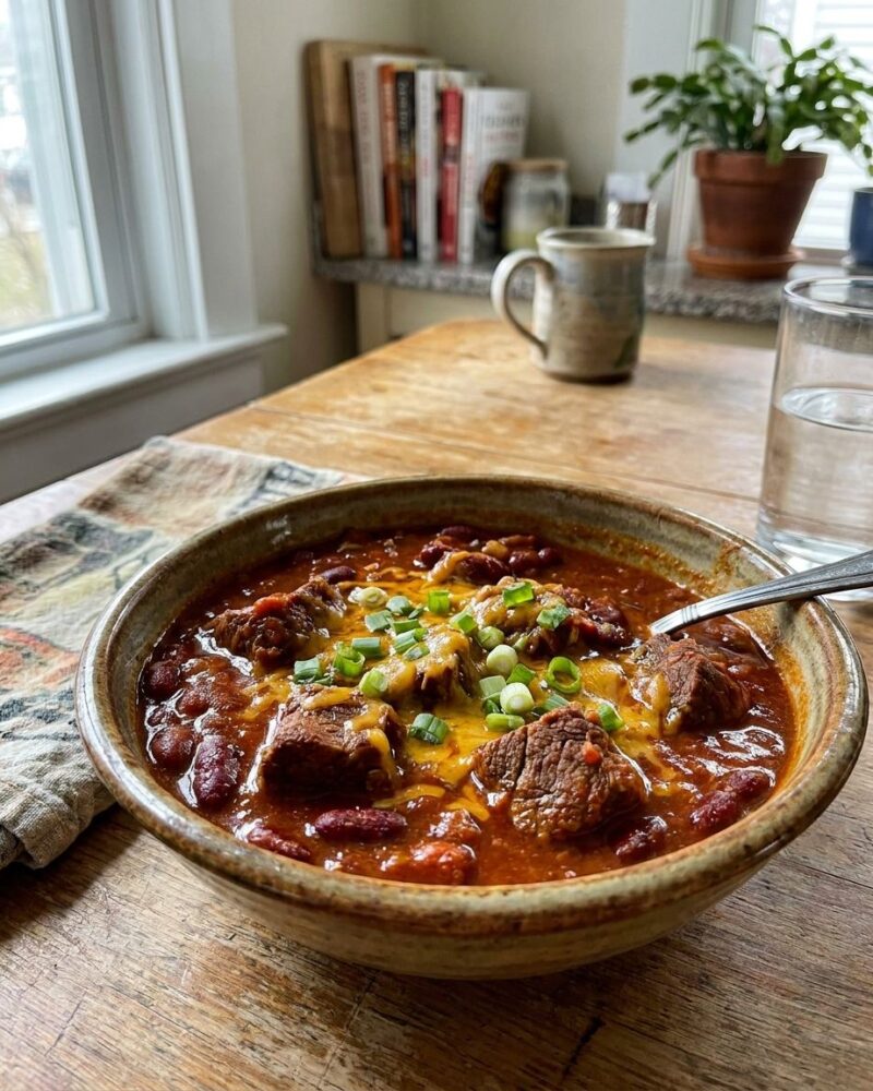 Bowl of chili con carne topped with cheese and scallions
